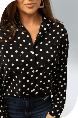 Woman wearing a black polka-dot button-up blouse with a classic touch and relaxed fit, showcasing versatile wardrobe style.